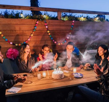 A group of six people celebrating a birthday with a birthday cake shows that transferring funds with Zelle is easy.