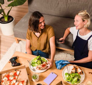 Two female friends share a pizza and a meal while splitting the expense using Zelle.